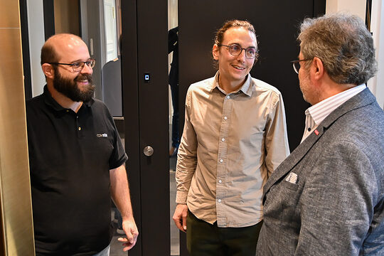 In einem Ausstellungsraum schauen sich drei Männer verschiedene Türmodelle an und unterhalten sich dabei.