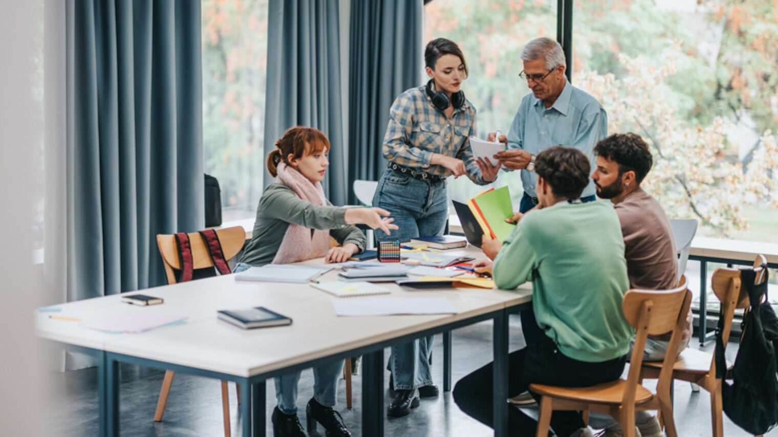 Ein Studententeam sitzt zur Teambesprechung am Tsch an der Hochschule und sprechen mit einem erfahrenem Mann.
