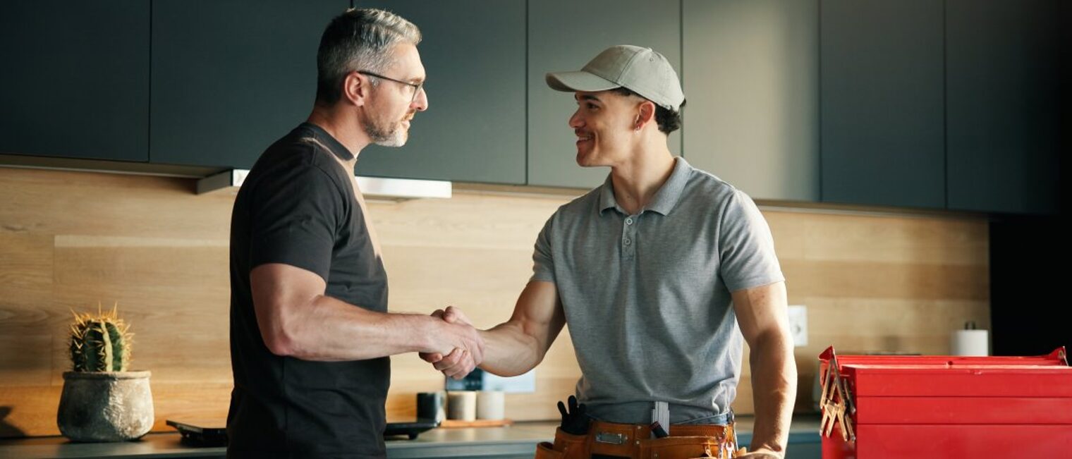 Zwei Männer stehen in einer Küche und reichen sich die Hand. 