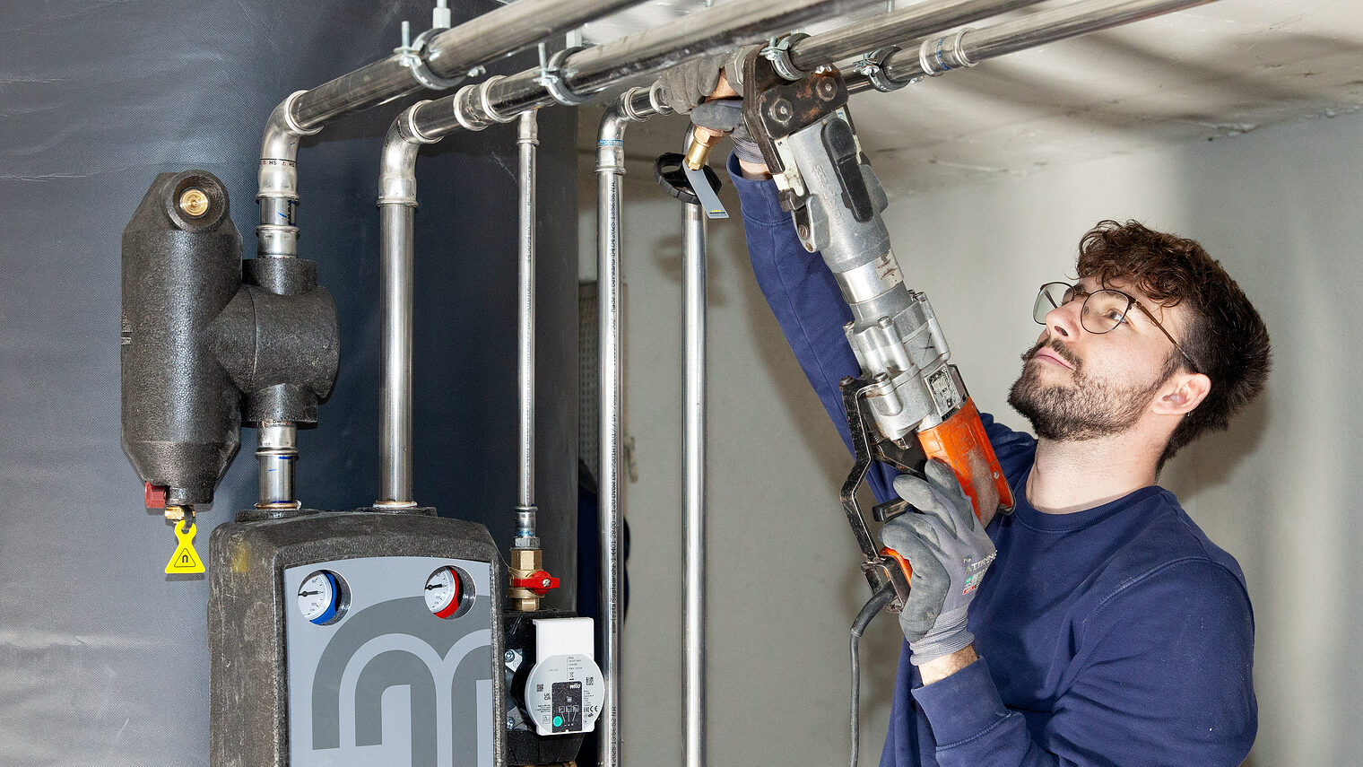 Ein steht in einem Heizungskeller und arbeitet an Rohren. 