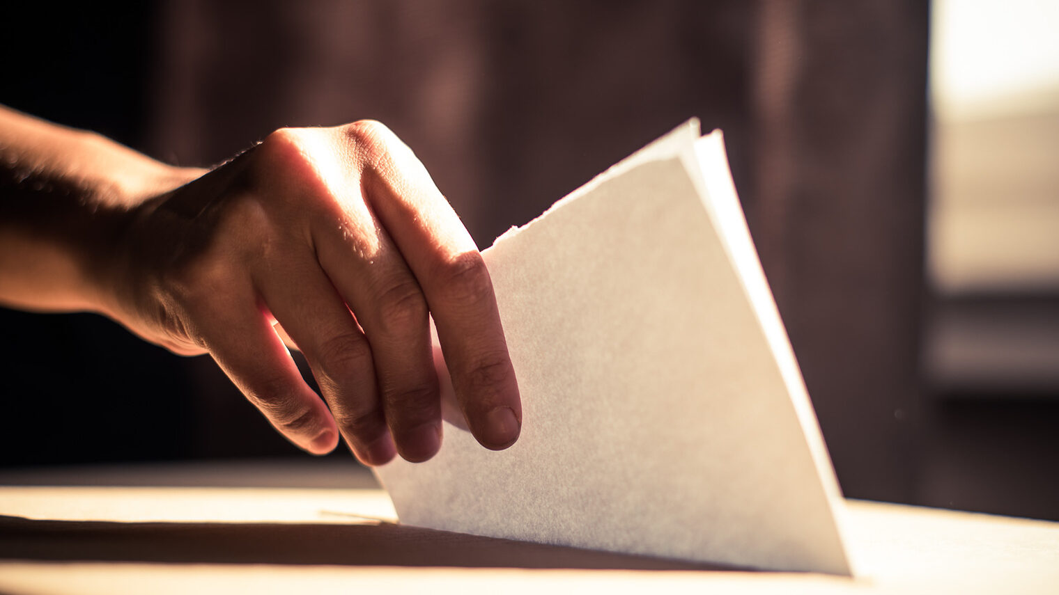 In Nahaufnahme ist zu sehen, wie jemand einen Stimmzettel in eine Wahlurne wirft.