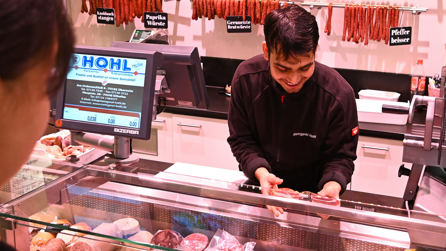 Ein Fleischereifachverkäufer-Azubi bedient in einer Metzgerei eine Kundin.