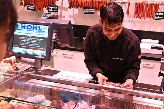 Ein Fleischereifachverkäufer-Azubi bedient in einer Metzgerei eine Kundin.