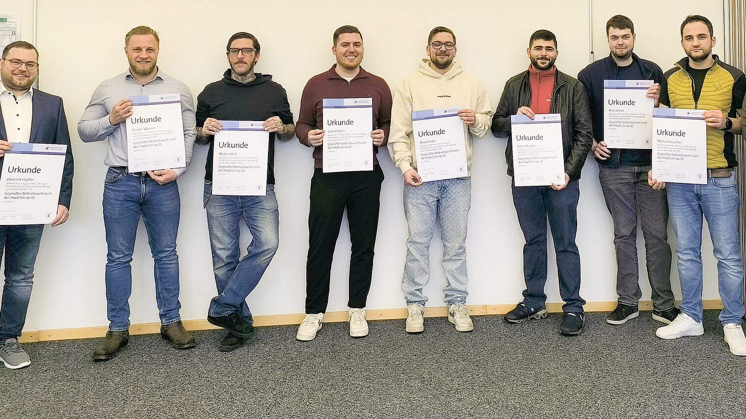 Zehn Männer stehen vor einer Wand und halten Urkunden in der Hand. 