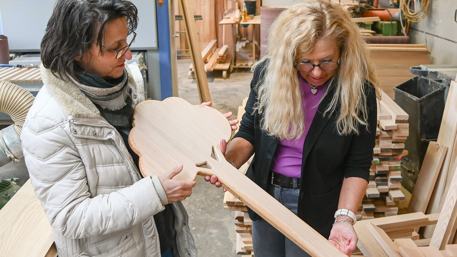 In einer Holzwerkstatt stehen zwei Frauen und schauen sich handgefertigten Grabschmuck aus Holz an.