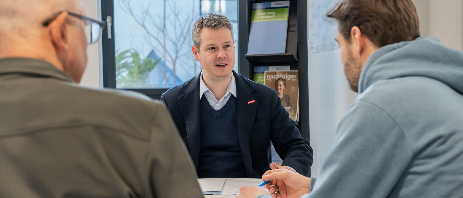 An einem Tisch sitzen drei Männer und unterhalten sich.