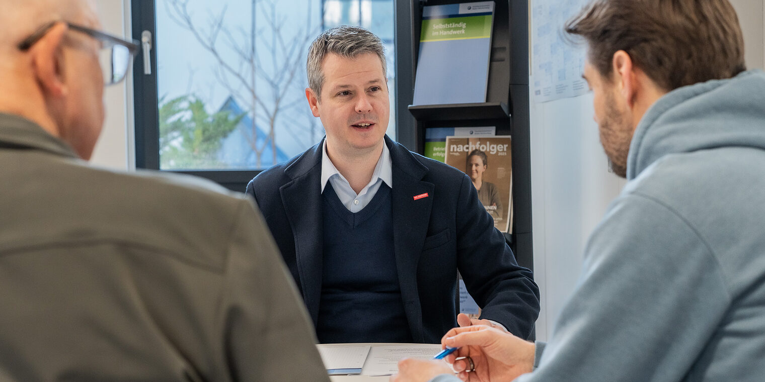 An einem Tisch sitzen drei Männer und unterhalten sich.