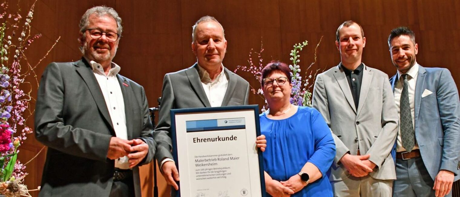 Vier Männer und eine Frau stehen auf einer Bühne. Ein Mann hält eine Urkunde in der Hand. 