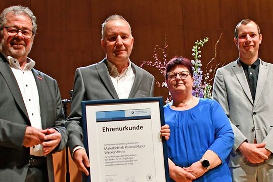 Vier Männer und eine Frau stehen auf einer Bühne. Ein Mann hält eine Urkunde in der Hand. 