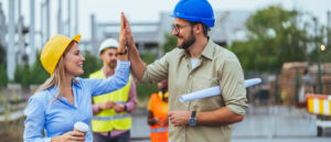 Eine Frau und ein Mann mit Schutzhelm geben sich auf einer Baustelle High Five.